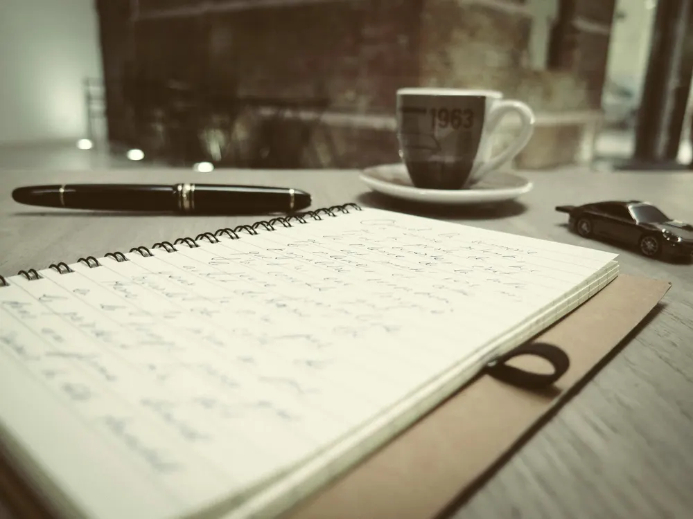 Een notitieboek met handgeschreven aantekeningen, een pen en een kop koffie