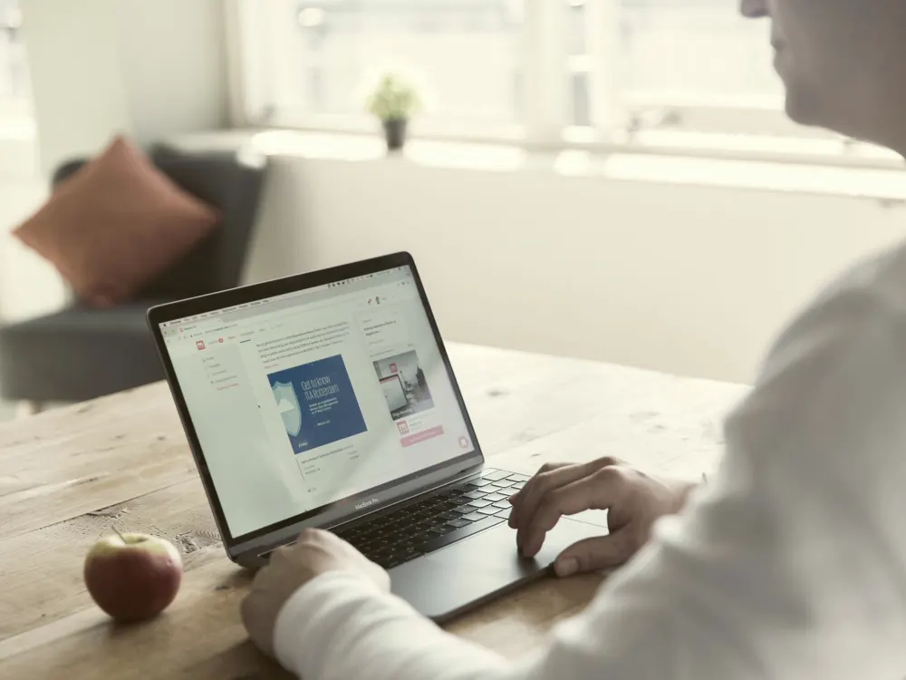 Iemand aan een houten tafel die iets op een laptopscherm bekijkt